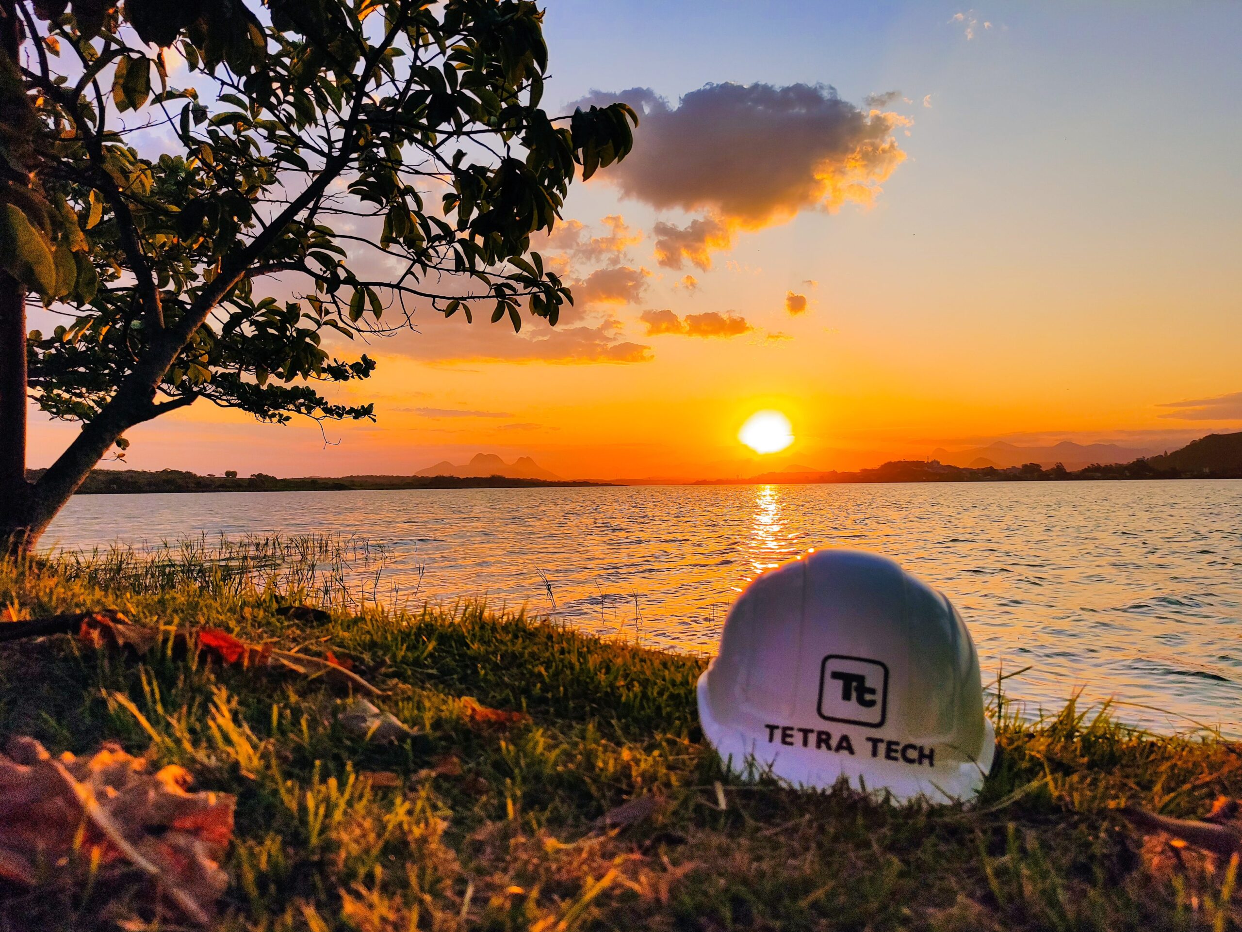 Capacete da Tetra Tech no chão, em frente ao mar, com um belo pôr do sol